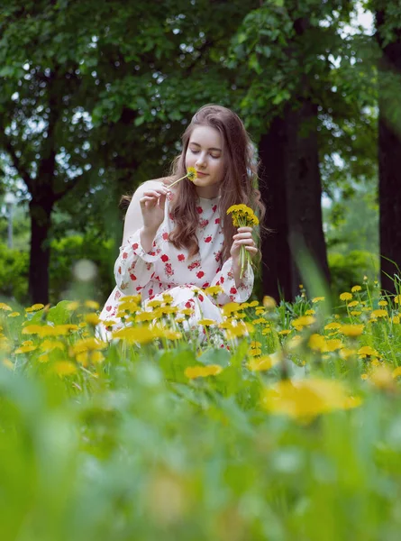 Uma linda garota loira em um vestido leve coleta um buquê de flores no parque em tempo ensolarado — Fotografia de Stock
