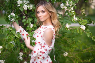 Açık renk saçlı, çiçekli bir bahçede açık renk elbiseli çekici bir genç kadın.