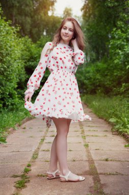 Beyaz açık renk elbiseli güzel bir kadın neşeyle yürüyor yaz kenti parkının yolunda..