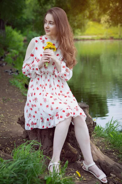 美丽的姑娘坐在湖边，手里拿着花 — 图库照片