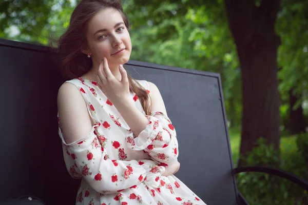 Beyaz elbiseli güzel bir kadın güneşli bir günde parktaki bankta oturuyor. — Stok fotoğraf