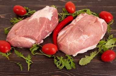 Ahşap arka planda çiğ domuz eti, domates, kırmızı biber ve taze otlar.