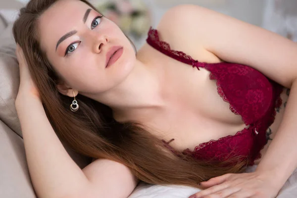一个温和的性感女人躺在床上，看着摄像机。穿着性感红色女士内衣的女孩. — 图库照片