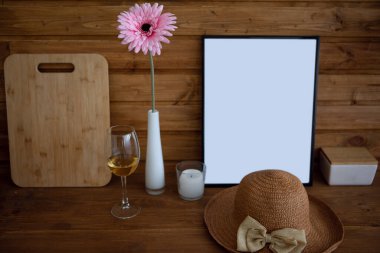 Bir bardak beyaz şarap, hasır bir şapka ve ahşap bir masada güzel bir çiçek..