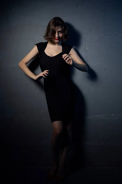 En sexig brunett i svart klänning lutad mot en grå stenmur i en provokativ pose — Stockfoto