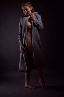 Güzel bir vücudu olan genç ve güzel bir kadın çıplak vücudunun üzerine örtünmüş bir sonbahar paltosuyla duruyor, başı ne yazık ki eğik..