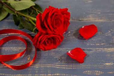 Büyük kırmızı gül tomurcukları hediye kurdelesi ve taç yapraklarıyla ahşap bir arka planda yatar. Sevgililer Günü 'nde ya da Anneler Günü' nde en sevdiğin kadınlar için bir hediye.