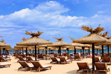 Sandy plaj çırpı ahşap şezlong ve şemsiye ile. Turistler rahatlayın ve dinlenme ve güneşin keyfini çıkarın.