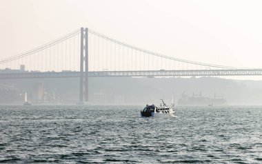 Bir deniz taşıtları ile 25 Tagus Nehri içinde de Abril Köprüsü ve Cristo Rei arka planda yelken.