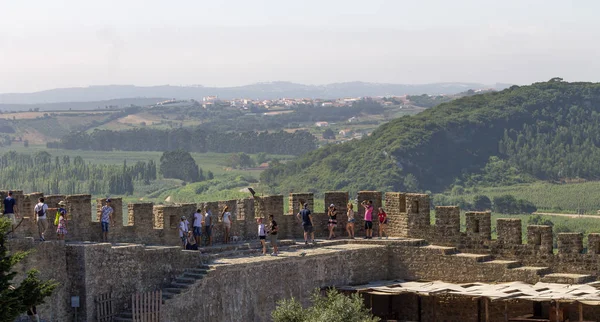 Several people stand along a castle\'s walls.