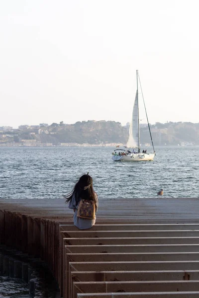 Een Meisje Zit Een Pier Terwijl Een Zeilboot Voorbij — Stockfoto