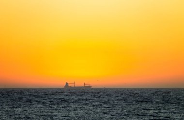 Bir kargo gemisi, görülür bir ufuk altın gökyüzünün ortasında.