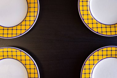 Dört sarı ve beyaz boş tabak siyah bir ahşap zemin.