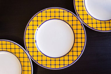 Üç sarı ve beyaz boş tabak siyah bir ahşap zemin.