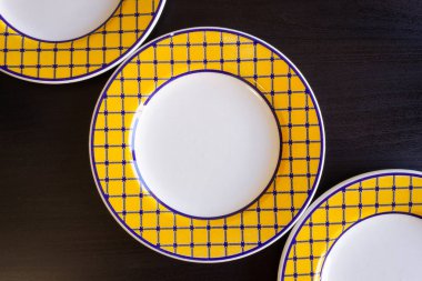 Üç sarı ve beyaz boş tabak siyah bir ahşap zemin.