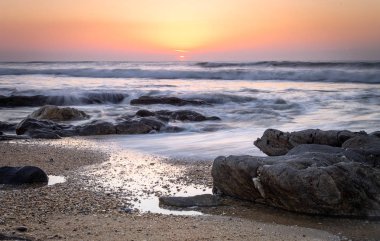 Kayalık plaj ve okyanus. Güneş ufukta ayarlar. Uzun pozlama. Açık gökyüzü. Altın saat. Kopya alanı.
