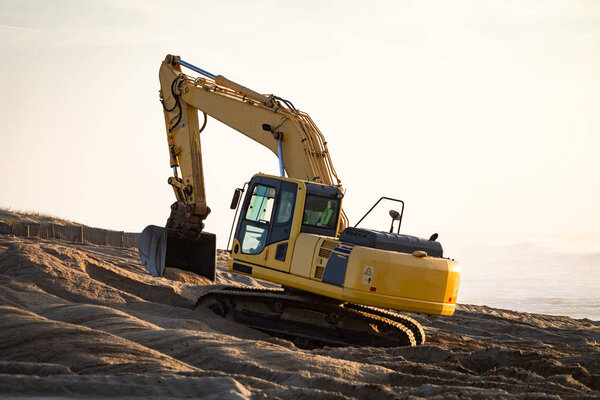 Yellow excavator gathers some sand at the beach. Warm light background. Copy space.