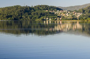 uzak binalar ve göl suya yansıtan yeşil tepeler
