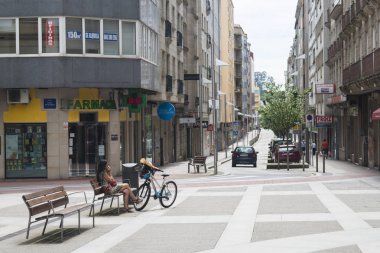 Pontevedra, İspanya - 11 Haziran 2017: Tahta bir bankta oturan bir kadın, yanında bisikletiyle cep telefonuyla konuşuyor.