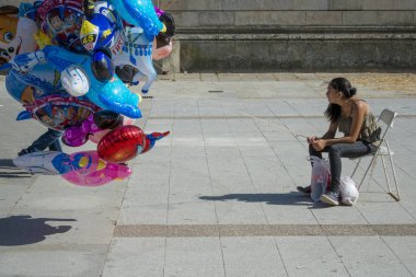 Pontevedra, Ispanya-3 Eylül 2016: bir sandalyede oturan genç bir kadın, şehirde kutlanan Ortaçağ Fuarı kutlama sırasında, caddenin ortasında balonlar satıyor.