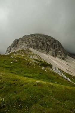 yeşil çayırlar ve kayalık tepede üzerinde bulutlu gökyüzü