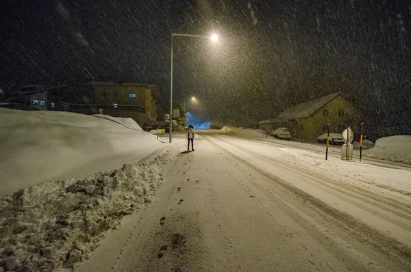 person standing by snowy road illuminated at night