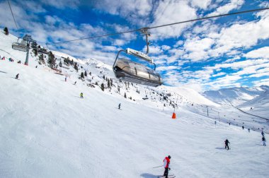 bulutlu gökyüzü altında karlı yamaçta kayak ile kayak asansörleri