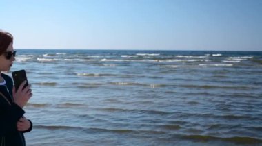 İş kadını telefonda konuşuyor ve sahilde yürüyüş güneş gözlüğü