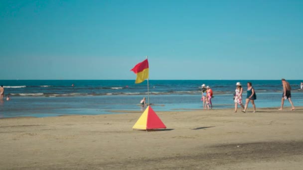 Röd och gul livet säkerhet flaggan blåser vinden med vissa personer på stranden — Stockvideo