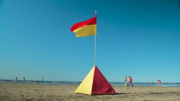 Hoofdredder veiligheid rood en geel vlag close-up met mensen en fietsen op strand — Stockvideo