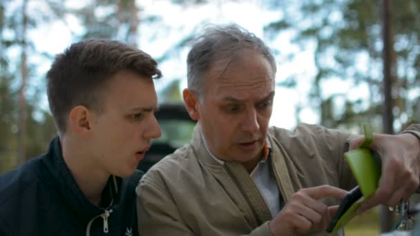 Father and son discussing a problem pointing at mobile phone and arguing outdoor — Stock Video