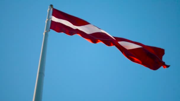 Bandera de Letonia en el enorme asta de la bandera soplando en el viento — Vídeo de stock