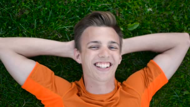 Feliz adolescente sonríe y habla con la cámara descansando en el césped de hierba al aire libre — Vídeo de stock