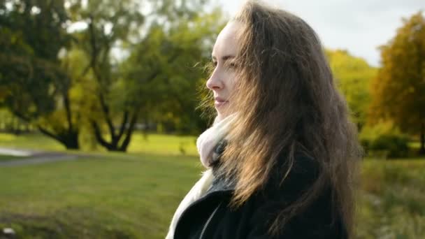 Bonita chica con hermoso pelo largo marrón se convierte en cámara caminando en el parque en otoño — Vídeos de Stock