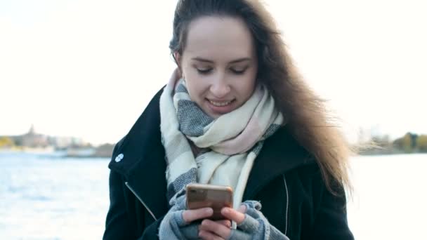 Chica bonita con hermosos mensajes de texto de pelo largo, utilizando el teléfono móvil al aire libre — Vídeo de stock