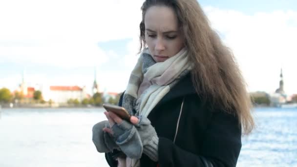 Pretty girl with beautiful long hair texting, using mobile phone smartphone outdoors with Old City on the background — Stock Video