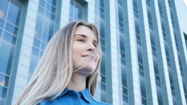 Low-angle portrait of a pretty girl with beautiful blue eyes and long hair with modern architecture on the background