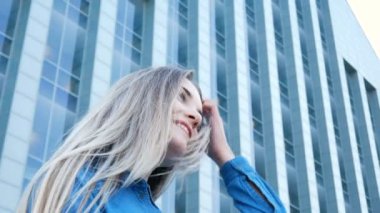 Low-angle portrait of a pretty girl with beautiful blue eyes and long hair with modern architecture on the background