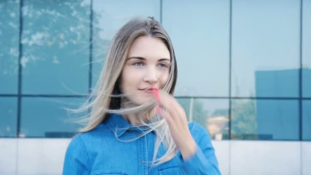 Portrait au ralenti d'une jolie fille aux beaux yeux bleus et aux cheveux longs à l'architecture moderne en arrière-plan — Video