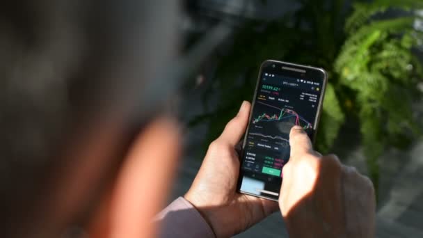 Zakenman is het controleren van Bitcoin prijsgrafiek op crypto Exchange op amobile telefoon scherm. Cryptocurrency Future prijs Voorspellings concept. — Stockvideo