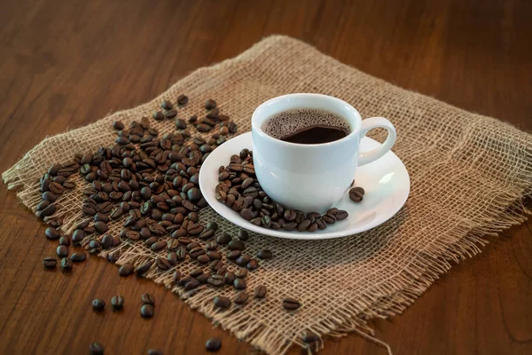 Гаряча чашка кави зі смаженими кавовими зернами на мішках та дерев'яному столі — стокове фото
