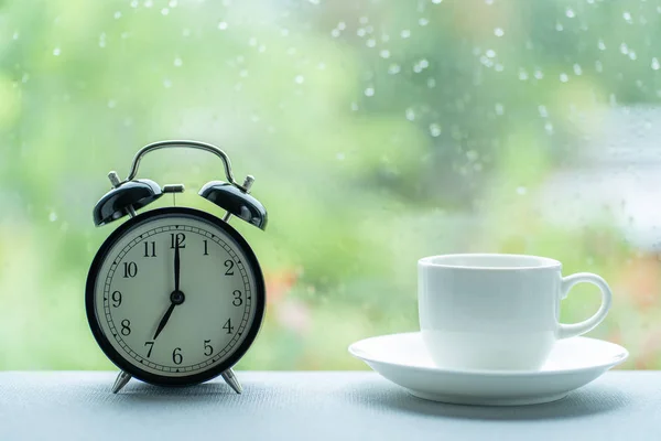 Чашка белого кофе и винтажные часы в семь часов на ра — стоковое фото