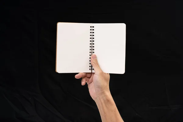 Mano de hombre sosteniendo cuaderno en blanco sobre fondo negro — Foto de Stock