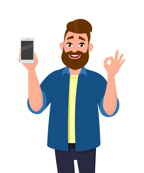 Χαρούμενος Νεαρός Άνδρας Δείχνει Smartphone Και Δείχνει Εντάξει Εντάξει Σημάδι — Διανυσματικό Αρχείο