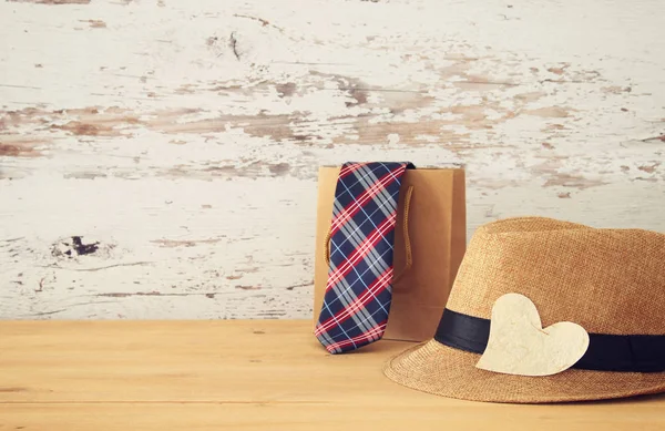 Bilden av manlig fedora hatt och shoppingväska med tie över träbord. . Fars dag-konceptet. — Stockfoto