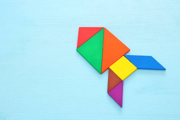 rocket made from tangram puzzle on blue pastel wooden background