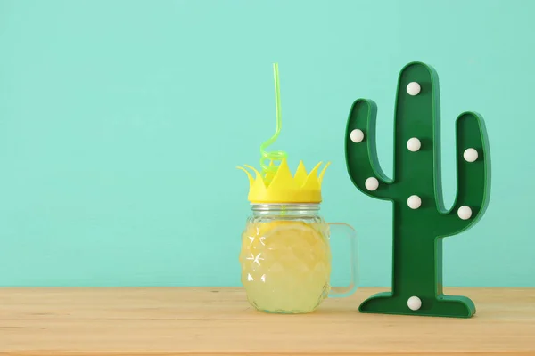 新鲜柠檬水饮料的图片在可爱的菠萝形状玻璃与扭曲秸秆旁边的塑料仙人掌在木桌上 — 图库照片