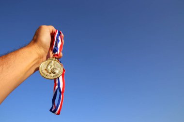 Adam el kaldırıyor, altın madalyayı gökyüzüne karşı tutuyor. ödül ve zafer konsepti