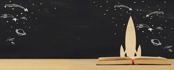 Вернемся к школьной концепции. Деревянные ракетные и космические эскизы над открытой книгой перед классной доской . — стоковое фото