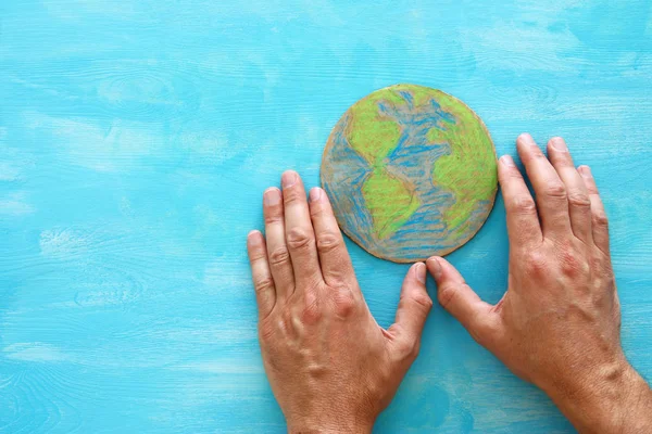 青い木製の背景上に地球を置く男の手の上から見たイメージ — ストック写真
